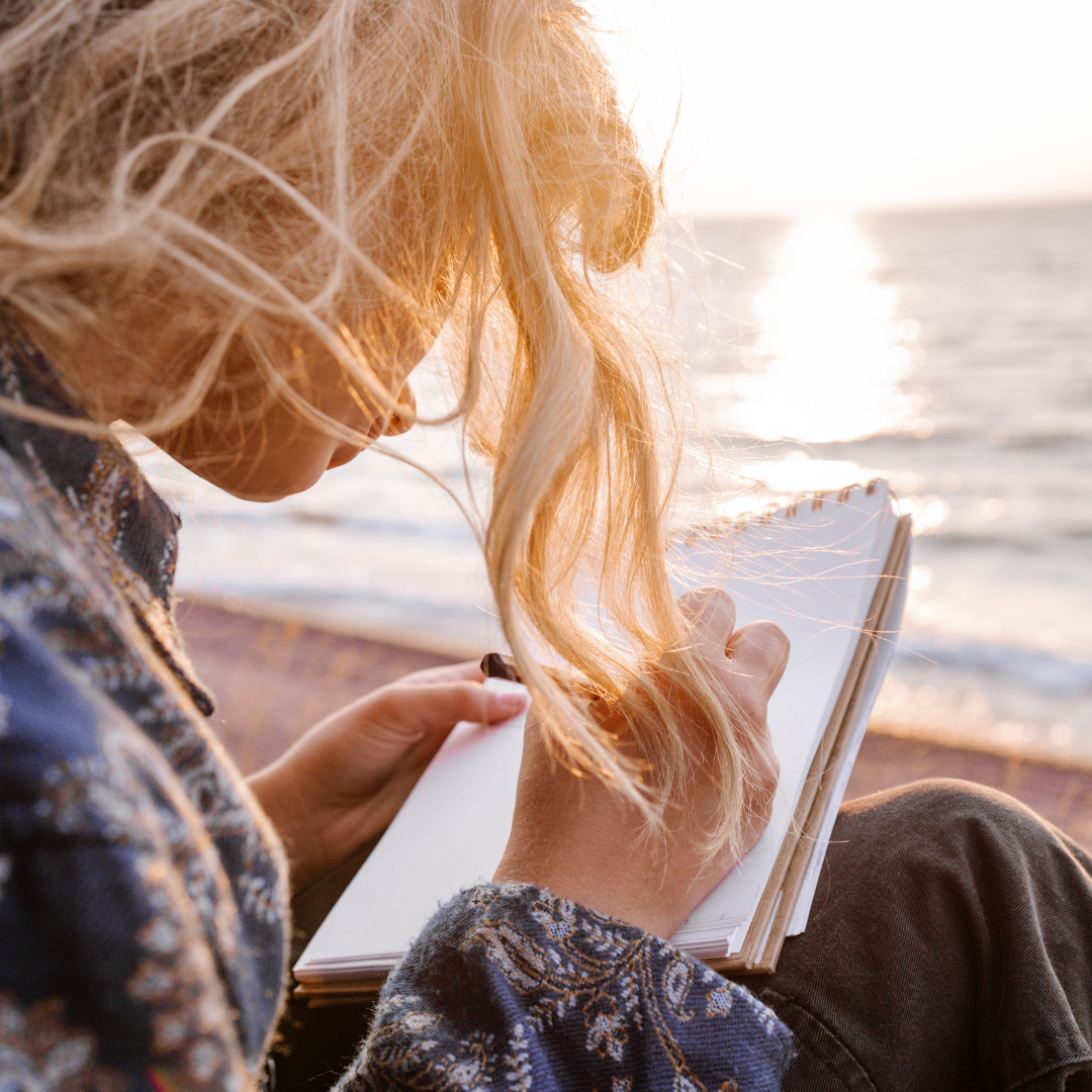 Woman on the beach with sunset writing with shadow work prompts