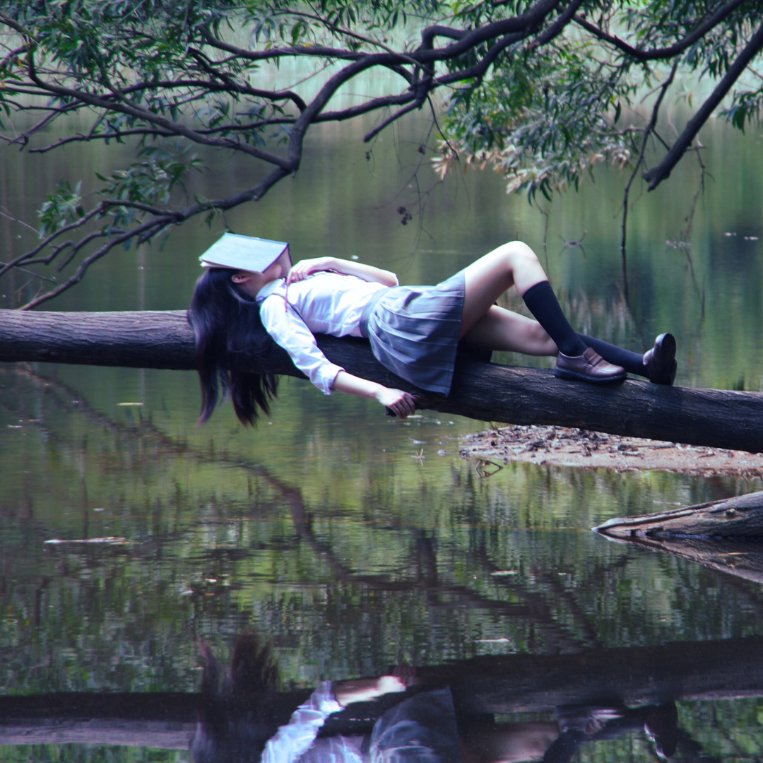 Woman laying on a log over a lake doing inner work with a journal