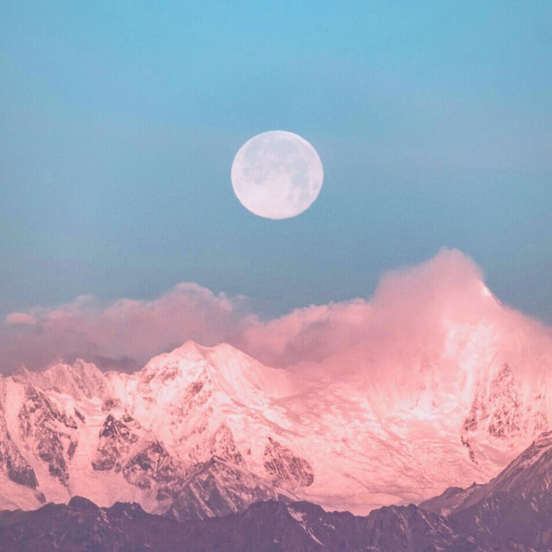 Full Moon rising over pink mountain into blue sky