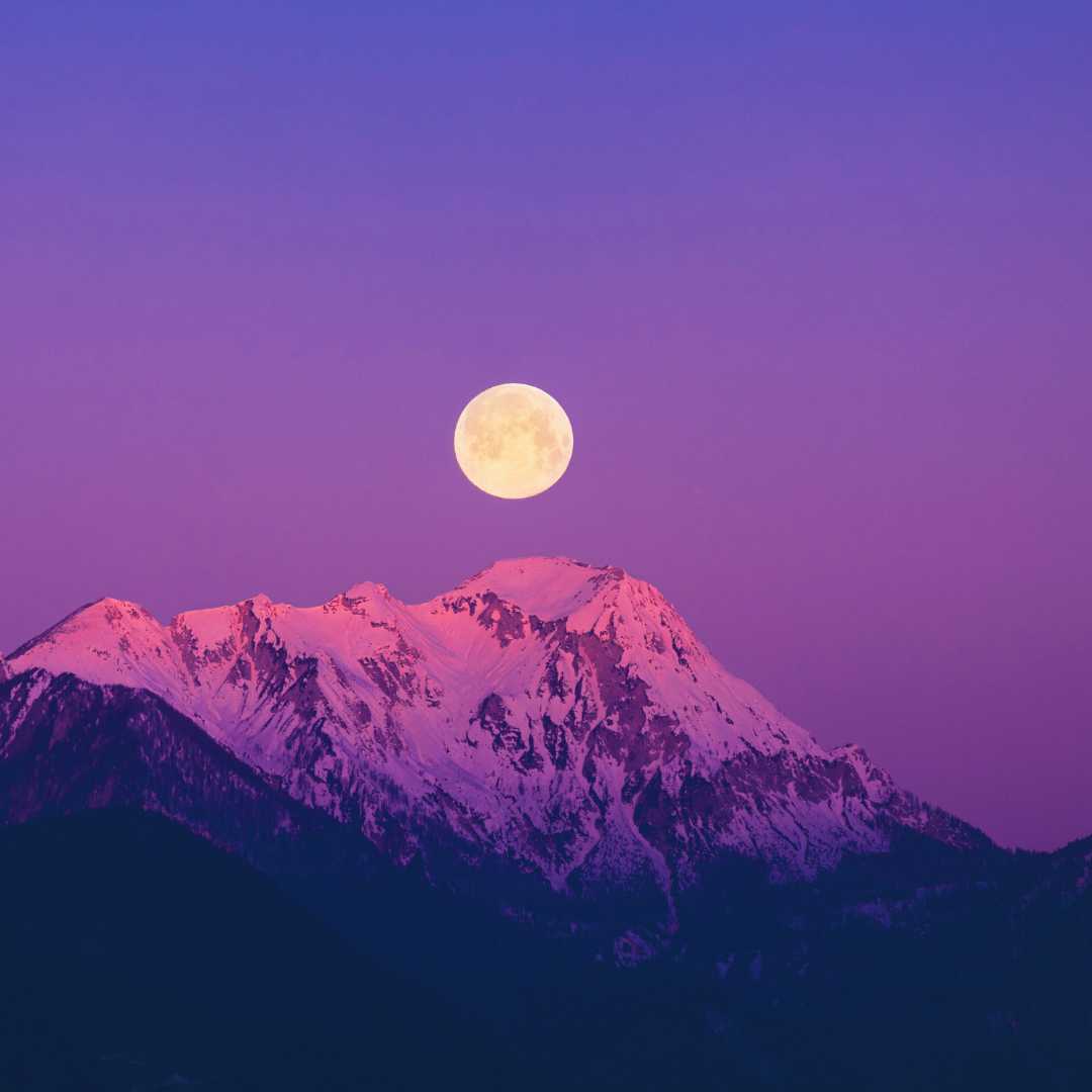 The next snow Moon rising over a mountain into a purple sky<br />
