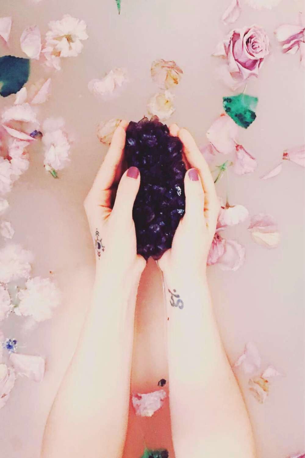 Beautiful dark purple crystal held in two hands over a milky spiritual bath
