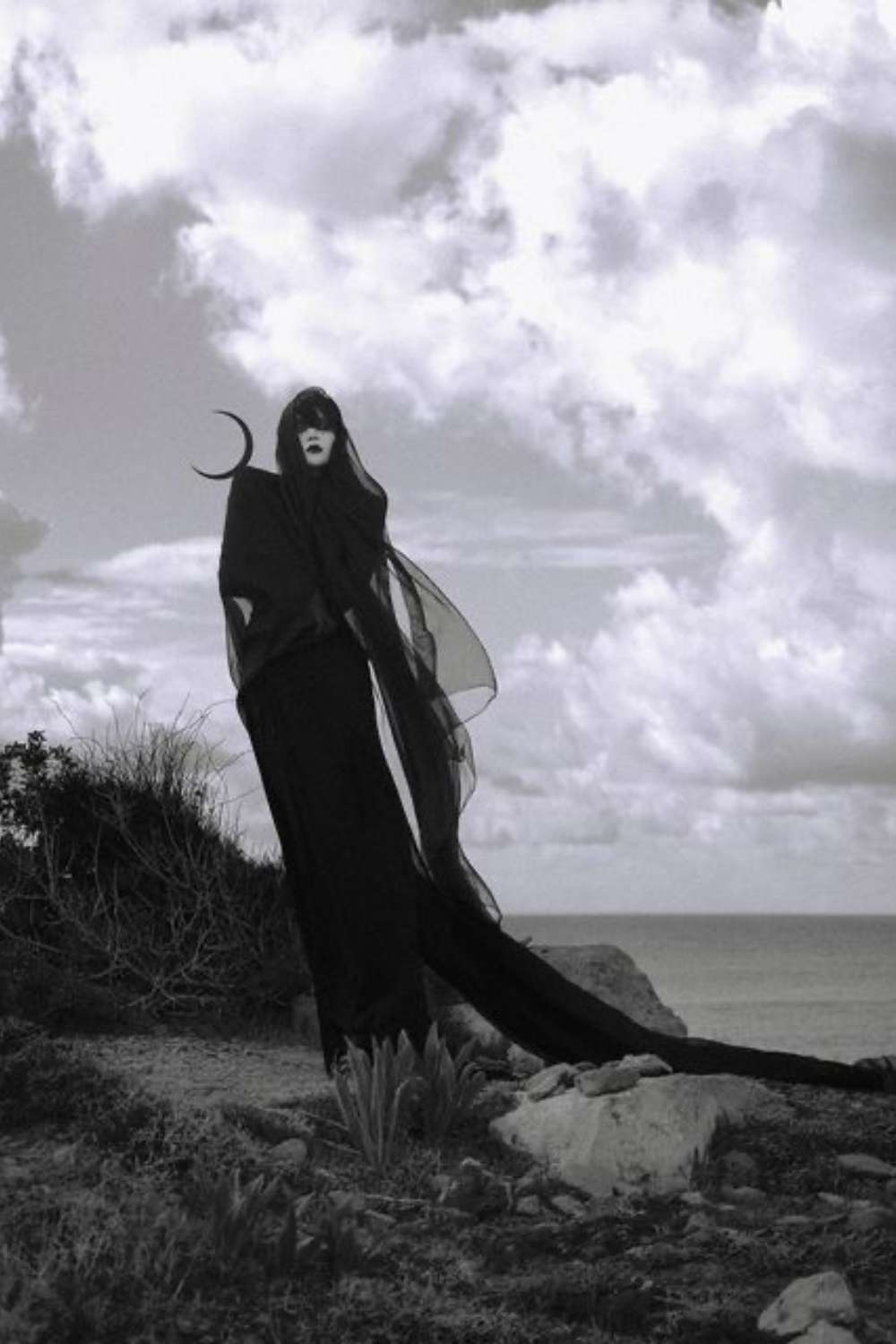 black and white image of dark feminine woman on a seashore with a crescent moon on her shoulder 